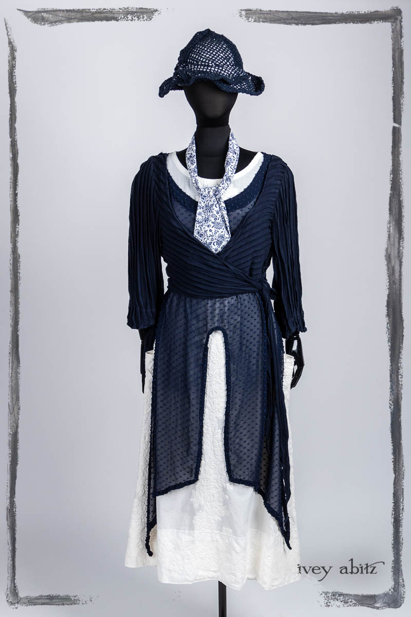 Vallonné Jacket in Bastille Blue Flutter Pleat Knit; Clotaire Sash in Bastille Blue Fleur Cotton; Lumiere Frock in Bastille Blue Tufted Dot Silk Chiffon; Limited Edition Covante Frock in Blanche Embroidered Stripe Voile; Hapgood Hat in Bastille Blue Open Weave Knit. Bespoke clothing by Ivey Abitz.