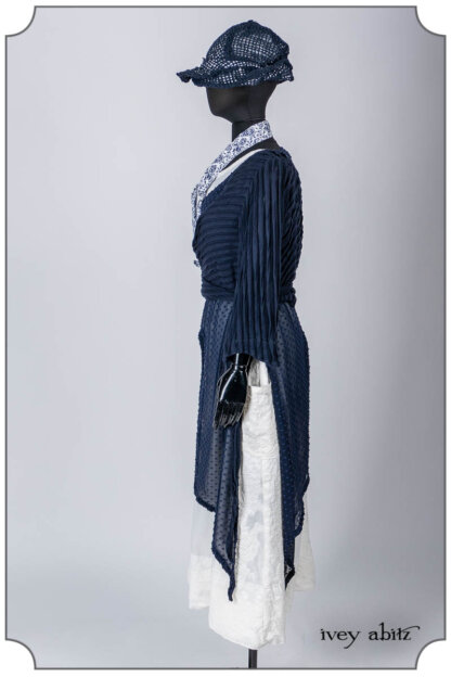 Vallonné Jacket in Bastille Blue Flutter Pleat Knit; Clotaire Sash in Bastille Blue Fleur Cotton; Lumiere Frock in Bastille Blue Tufted Dot Silk Chiffon; Limited Edition Covante Frock in Blanche Embroidered Stripe Voile; Hapgood Hat in Bastille Blue Open Weave Knit. Bespoke clothing by Ivey Abitz.