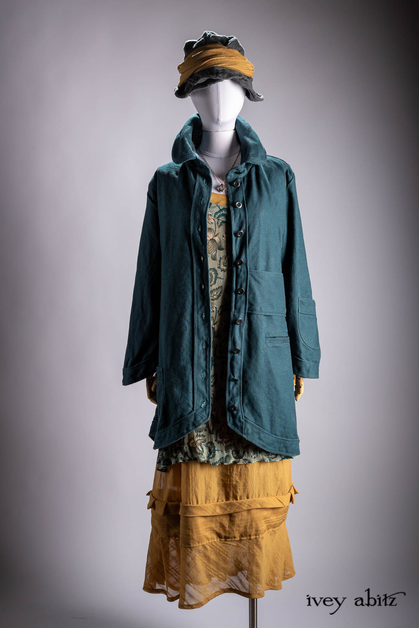 Ellis Duster Coat in Idyllic Green Woven Weave; Pierrepont Shirt in Crimson Three-Leaf Silk; Liberte Frock in Riverbank Floral Woven Weave; Cilla Slip Frock in Bark Silky Knit; Hapgood Hat in Bark Washed Woven Hat Weave; Nouvelle Necklace.