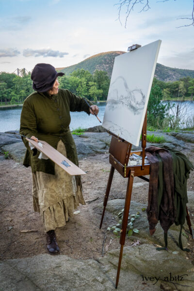 Ellis Shirt in Idyllic Green Puckered Voile; Liberte Frock in Riverbank Floral Woven Weave; Cilla Slip Frock in Bark Silky Knit; Hapgood Hat in Bark Washed Woven Hat Weave. On painting easel: Ellis Duster Coat in Idyllic Green Washed Woven Weave; Baedeker Scarf in Bark Mottled Mohair Hat and Scarf Knit.