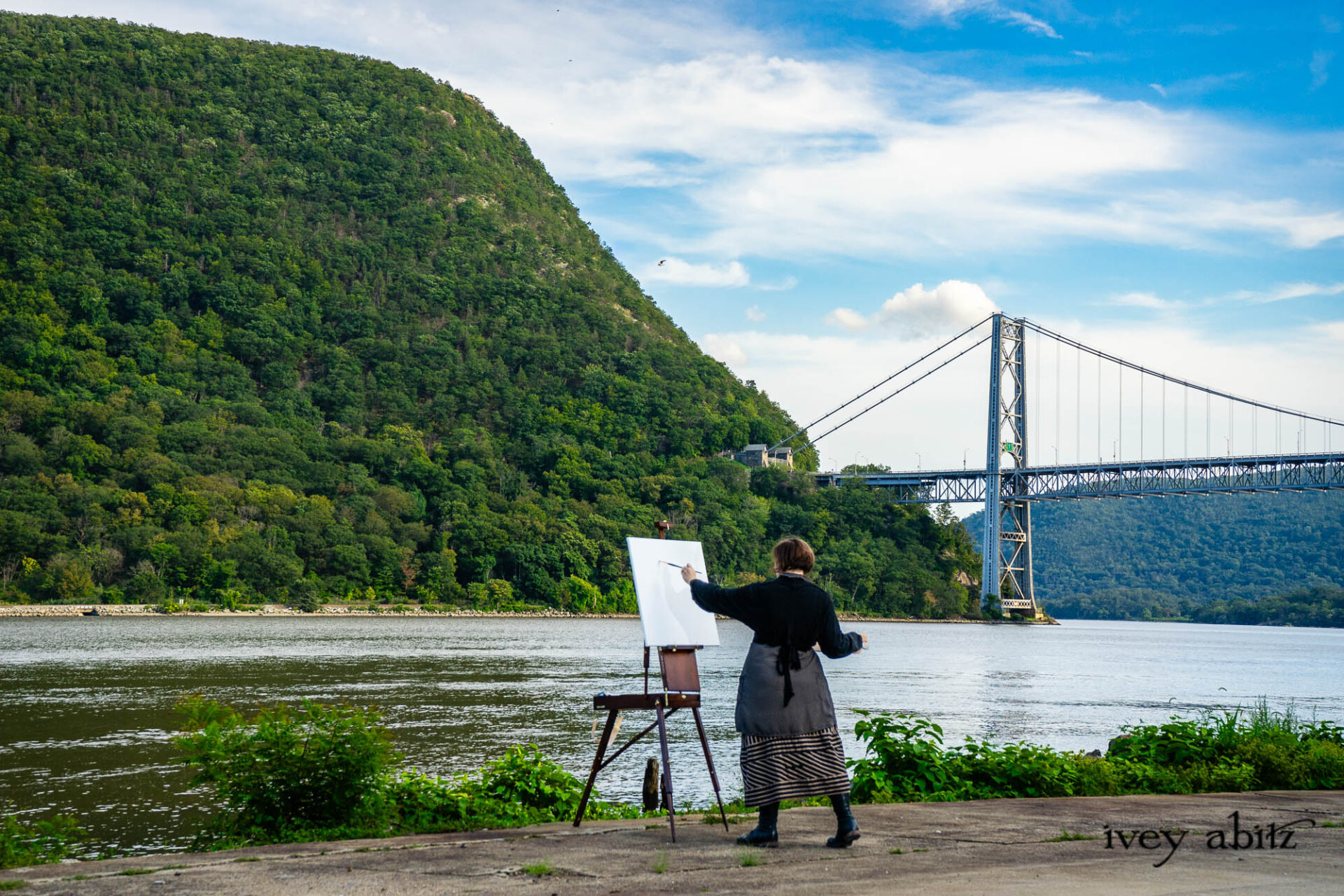 Cynthia Ivey Abitz painting Anthony's Nose and the Bear Mountain Bridge on location in the Hudson Valley. bEugenia Jacket in Mountain Mottled Ribbed Knit Baedeker Shirt Jacket in Mountain and Riverbank Petite Dot Silk Harbourhill Tie in Mountain and Riverbank Puckered Dot Cotton Baedeker Frock in Mountain and Riverbank Stripe Silk Hapgood Hat in Black Plaid Hat Weave Nouvelle Necklace