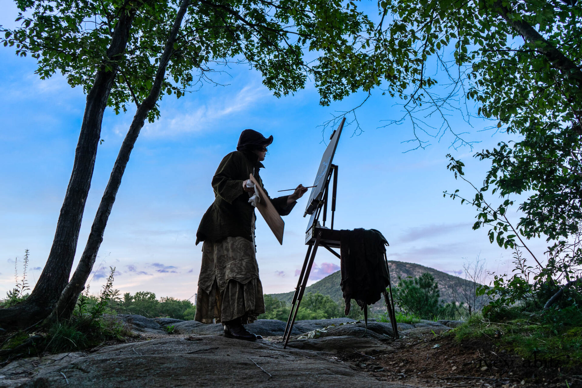 Cynthia Ivey Abitz painting Hessian Lake on location. Ellis Shirt in Idyllic Green Puckered Voile Liberté Frock in Riverbank Floral Woven Weave Cilla Slip Frock in Bark Silky Knit Hapgood Hat in Bark Washed Woven Hat Weave Baedeker Scarf in Bark Mottled Mohair Hat and Scarf Knit On painting easel: Ellis Duster Coat in Idyllic Green Washed Woven Weave