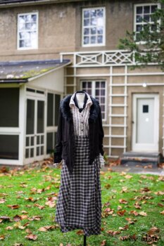 Limited Edition Coulson Cardigan in Dignity Soutache Knit; Pierrepont Shirt in Dignity Washed Vine Silk; Fairholme Necktie in Unity Washed Linen; Fairholme Skirt in Dignity Plaid Cotton. Location: In front of Eleanor's office where she wrote many books, letters, and the newspaper column "My Day." Location: Eleanor Roosevelt National Historic Site. Val-Kill, Hyde Park, New York.