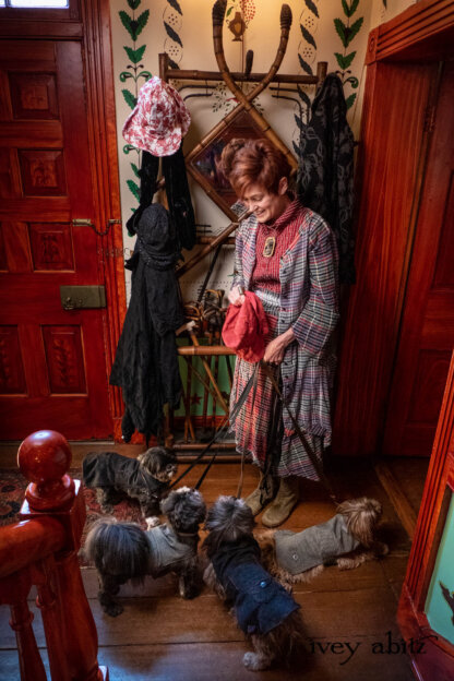 Highlands Shirt in Ruby Embroidered Stripe Silk; Bonheur Brooch in Ruby Sculpted Felt; Highlands Duster Coat in Gem Softest Plaid Wool; Highlands Skirt in Gem Softest Plaid Wool; Nouvelle Necklace. - Bespoke clothing by Ivey Abitz. Featuring Carolyn Hennesy with rescue dogs and cats.