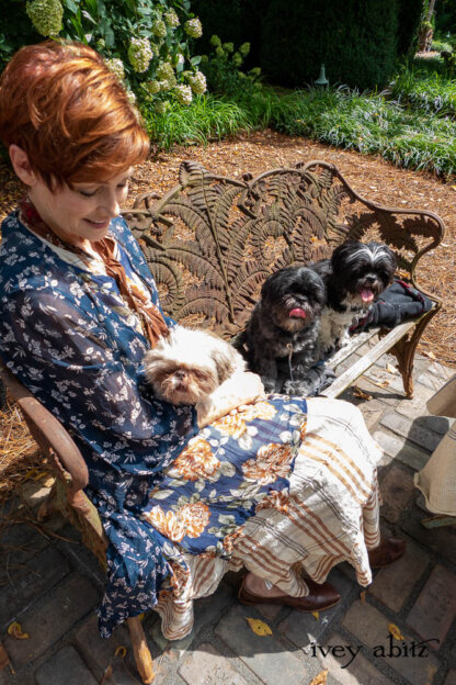 Lumiere Jacket in Blue Kyanite Petite Floral Silk Chiffon; Bedloe Frock in Blue and Copper Floral Silk Chiffon; Heraldry Frock in Copper and Pearl Plaid; Clotaire Sash in Copper Petite Floral Silk Chiffon; Nouvelle Necklace. - Bespoke clothing by Ivey Abitz. Featuring Carolyn Hennesy with rescue dogs and cats.