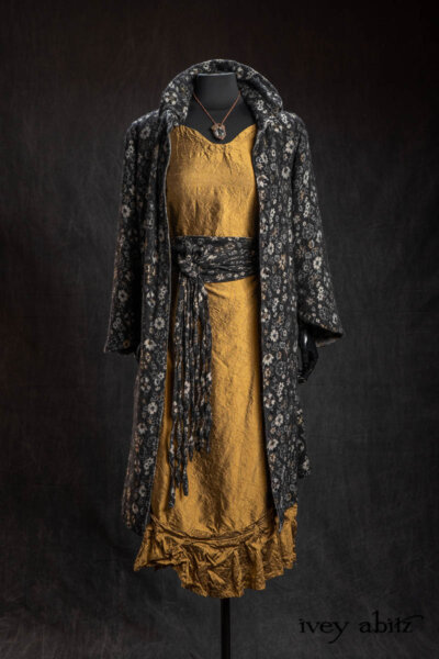 Limited Edition Phinneus Coat in Black Diamond and Pewter Floral Brocade; Porte Cochere Sash in Black Diamond and Pewter Floral Brocade; Inglenook Frock in Brass Crushed Silk; Cilla Slip Frock in Signature Black Washed Silk Jersey Knit; Heirloom Necklace. - Bespoke clothing by Ivey Abitz.
