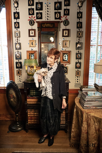 Truitt Duster Coat in Black Diamond Daisy Stretch Knit; Truitt Vest in Pearl and Black Diamond Sumptuous Knit; Truiit Shirt in Pearl Floral Crepe de Chine; Fitz Necktie in Black Diamond Embroidered Daisy Voile; Lydia Trousers in Black Diamond Silk Velvet; Voyage Satchel in Black Diamond Faux Fur. - Bespoke clothing by Ivey Abitz. Featuring Carolyn Hennesy with rescue dogs and cats.