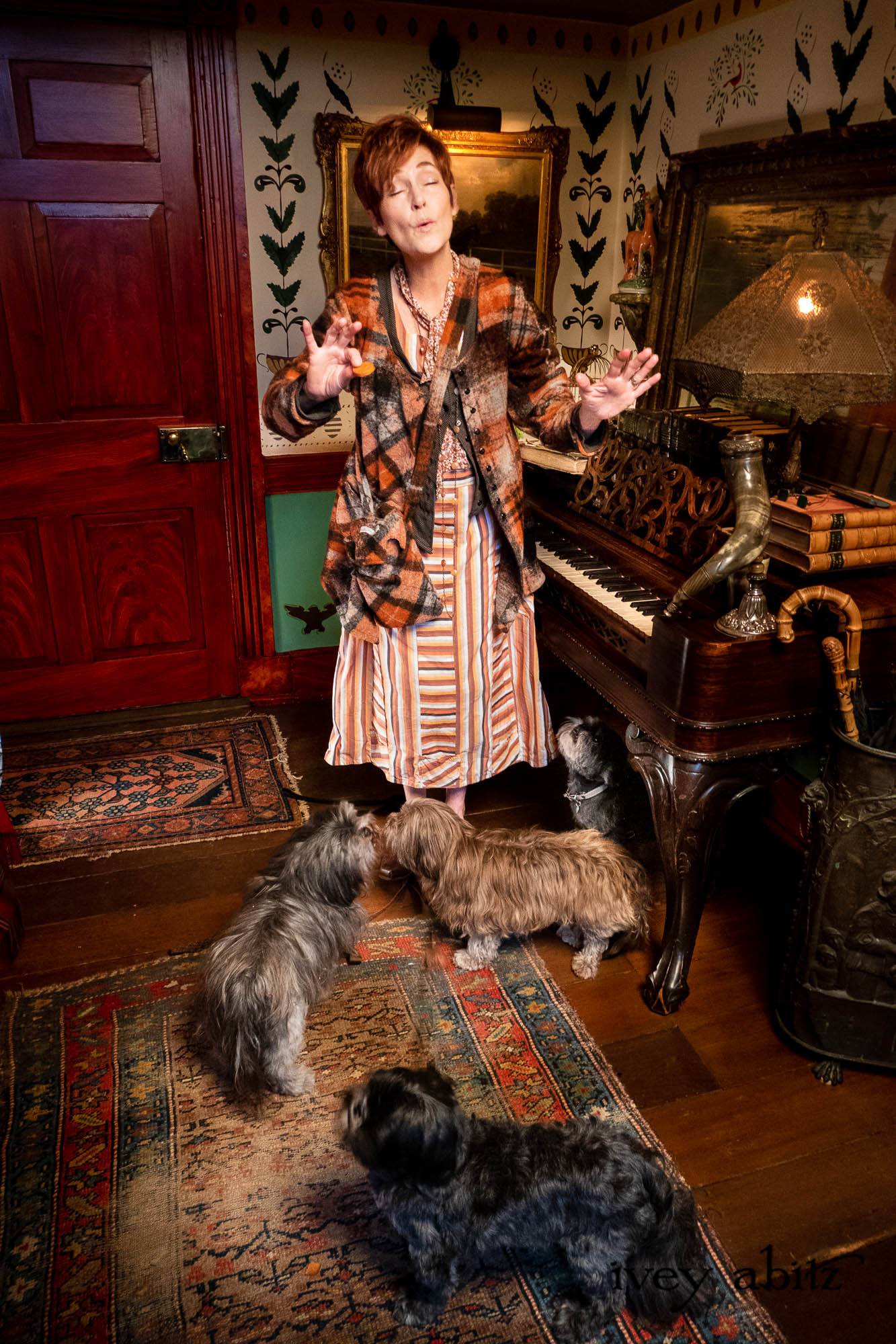 Limited Edition Gilbert Cardigan in Earth and Iron Petite Stripe Knit; Meriwether Frock in Copper Softest Plaid Twill; Essentielle Frock in Copper Petite Fleur Knit; Nouvelle Necklace; Elliot Vest in Copper Argyle Knit; Highlands Sash in Copper Petite Fleur Knit. - Bespoke clothing by Ivey Abitz. Featuring Carolyn Hennesy with rescue dogs and cats.