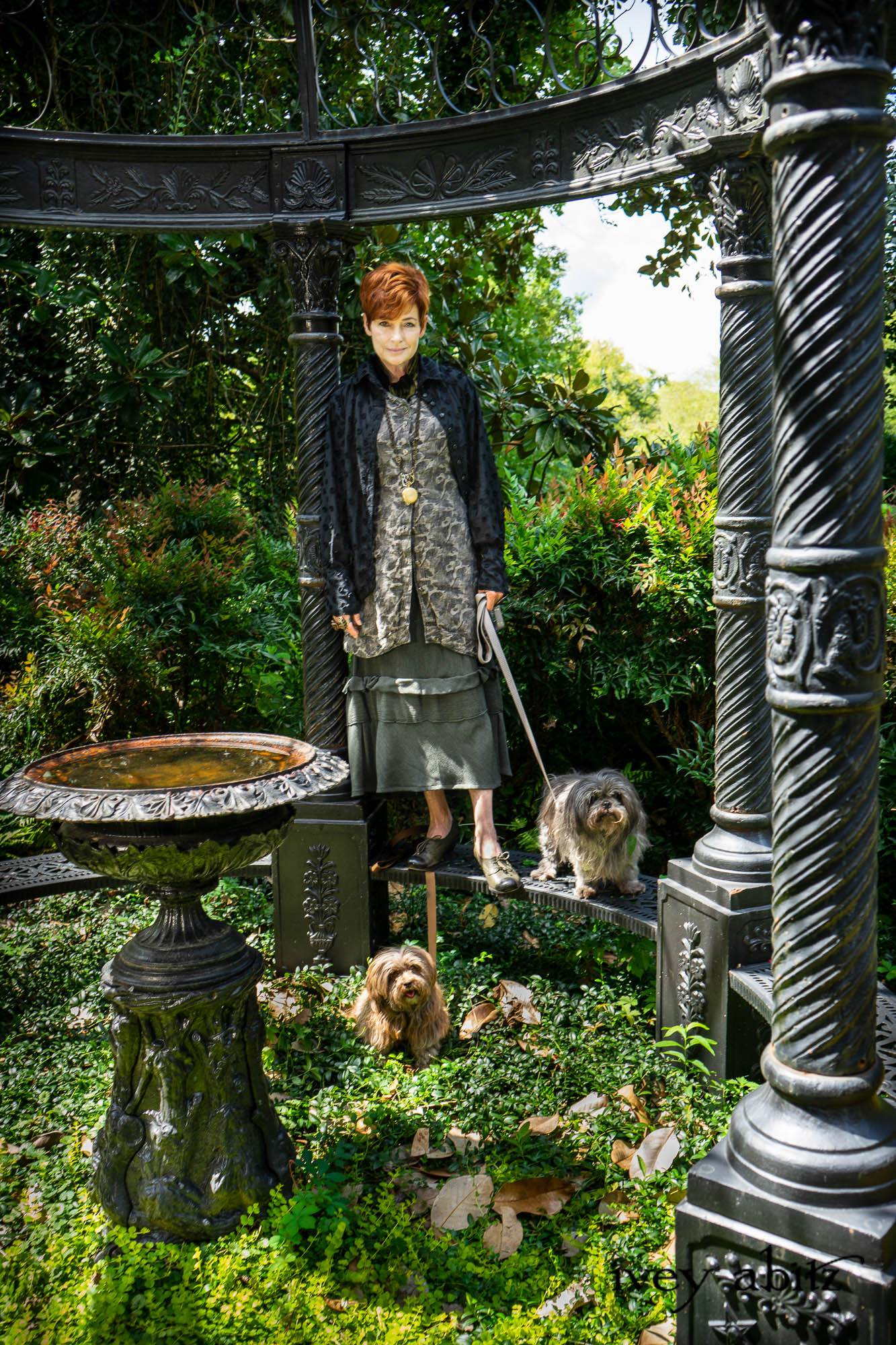 Truitt Duster Coat in Black Diamond Daisy Stretch Knit; Baedeker Scarf (Petite) in Black Diamond Silk Velvet; Hapgood Hat in Black Diamond Crushed Velvet; Nouvelle Necklace; Truitt Frock in Pewter and Stone Floral Linen; Hudson Frock in Olive Quartz Crinkled Weave. - Bespoke clothing by Ivey Abitz. Featuring Carolyn Hennesy with rescue dogs and cats.